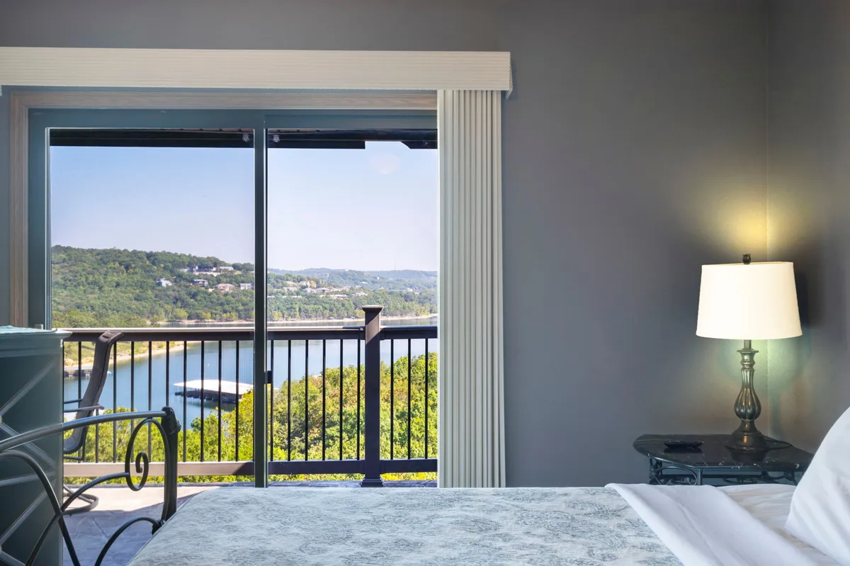 A serene bedroom with a comfortable bed positioned beside a large window that frames a panoramic view of the water. The soft lighting and uncluttered nightstand evoke a sense of tranquility and an invitation to relax while taking in the scenery.