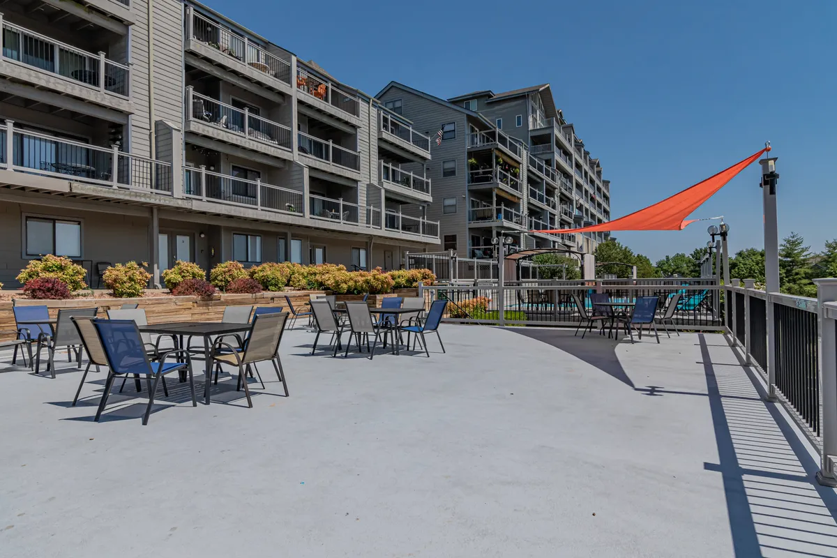 A vibrant exterior scene featuring an outdoor seating area with colorful umbrellas, landscaped flower beds, and the building’s inviting facade. The area is set up for families or groups to relax, socialize, or enjoy outdoor meals together.