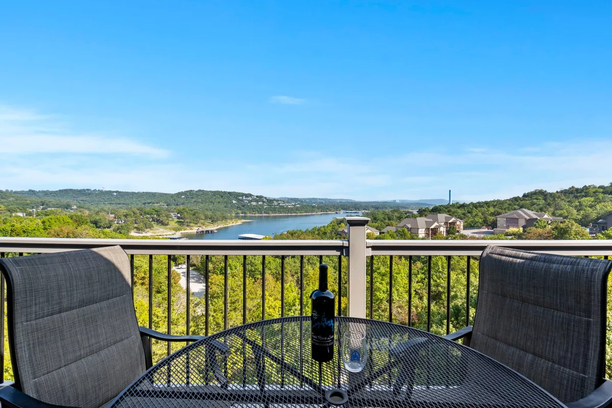 A deck or patio space set with a table, wine bottle and glass, overlooking a breathtaking water view and lush greenery. The atmosphere is tranquil, perfect for morning coffee or sunset toasts just steps from indoors.