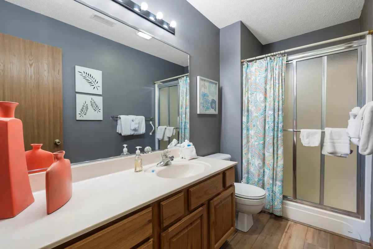 A tranquil bathroom scene with a stylish vanity adorned with coral vases, aquatic-themed art, and a decorative shower curtain. The soft lighting and inviting decor create a peaceful setting for self-care routines.