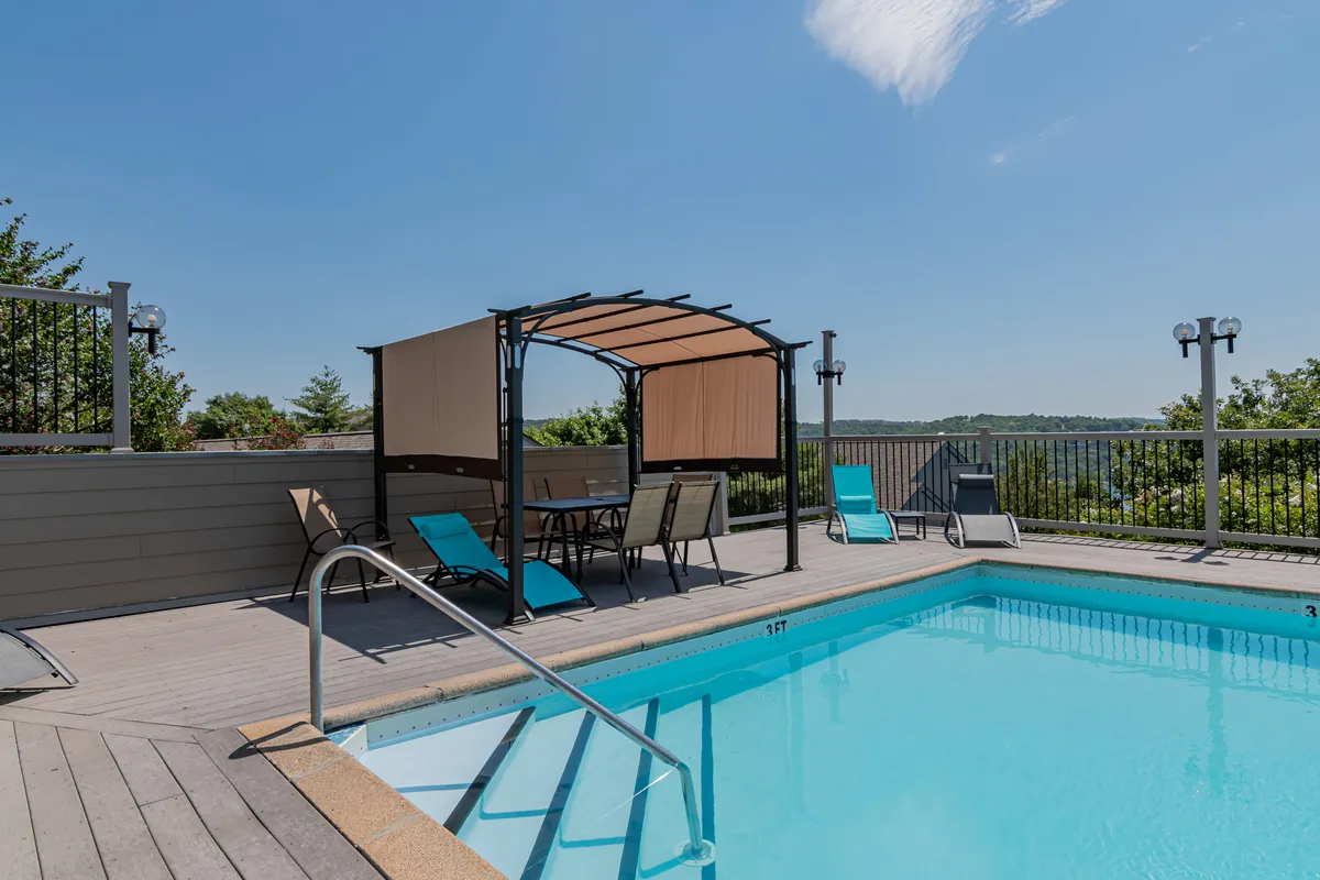 A sunny exterior view of a sparkling swimming pool surrounded by lounge chairs and a canopy, with families and groups enjoying leisure time in and around the water.