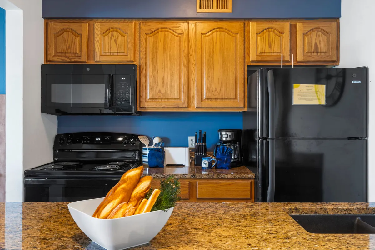 The image captures a cozy kitchen corner with a granite countertop, a bowl of fresh bread, and visible modern appliances. The scene feels inviting and homey, ideal for showcasing intimate meals or prepping food for a group.