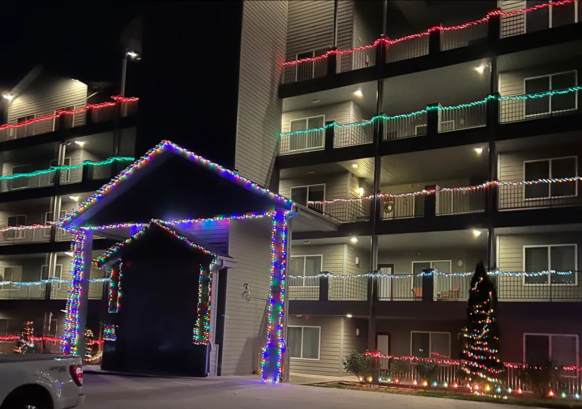 This exterior image showcases the entrance to the condo building beautifully decorated with colorful Christmas lights and illuminated balconies, creating a festive and welcoming atmosphere. The scene captures the building's accessibility and hints at the communal, resort-like setting residents and guests enjoy.