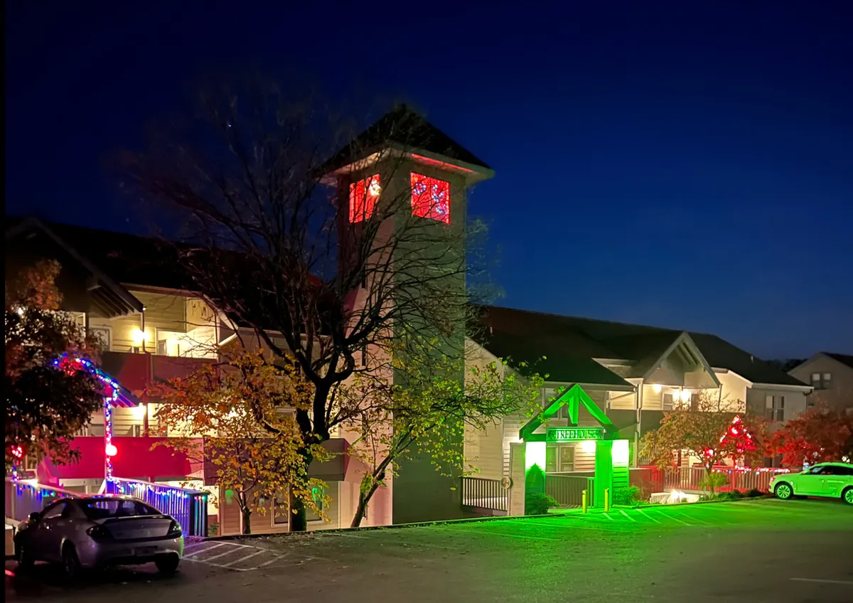 An exterior shot featuring a distinctive tower with illuminated windows, a green entrance sign, and decorative lighting on the building. The evening lighting and signage highlight the property's recognizable features and approachable, inviting entry point.