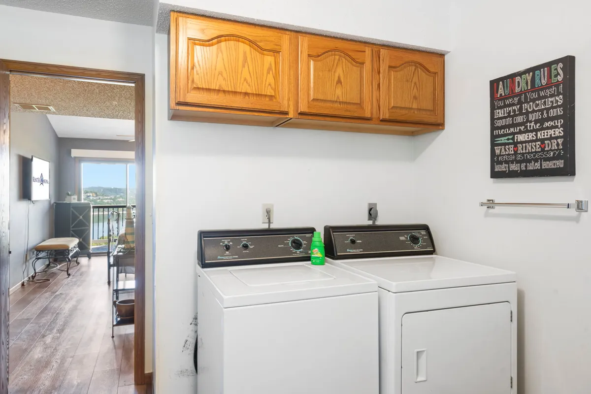 A practical laundry area featuring a washing machine, dryer, and wooden cabinets, complemented by a 'laundry rules' sign for a homey touch. The setup is both functional and welcoming, ideal for extended stays.
